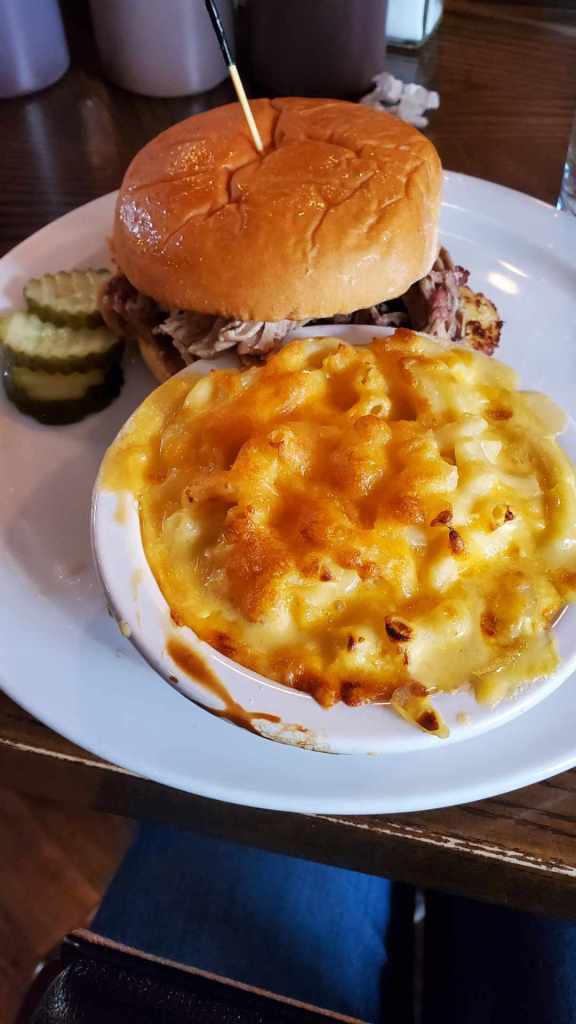 [Image is a BBQ pork sandwich with two pickles and a bowl of cheddar mac and cheese.]